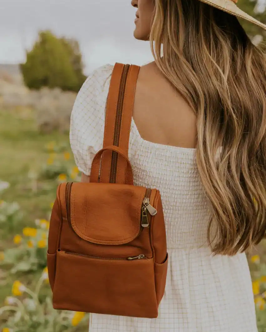 Mini sac à dos en cuir marron avec une rabat en haut et des zippers dorés.