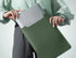 Person insérant un ordinateur portable en cuir dans une pochette de protection verte foncée