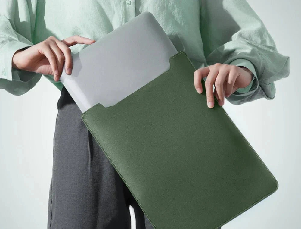 Person insérant un ordinateur portable en cuir dans une pochette de protection verte foncée