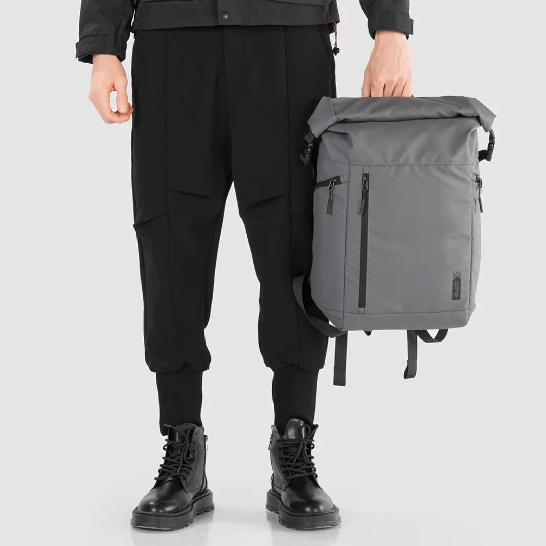 Person tenant un sac à dos Nebula XB gris à fermeture rouleau avec poches zippées