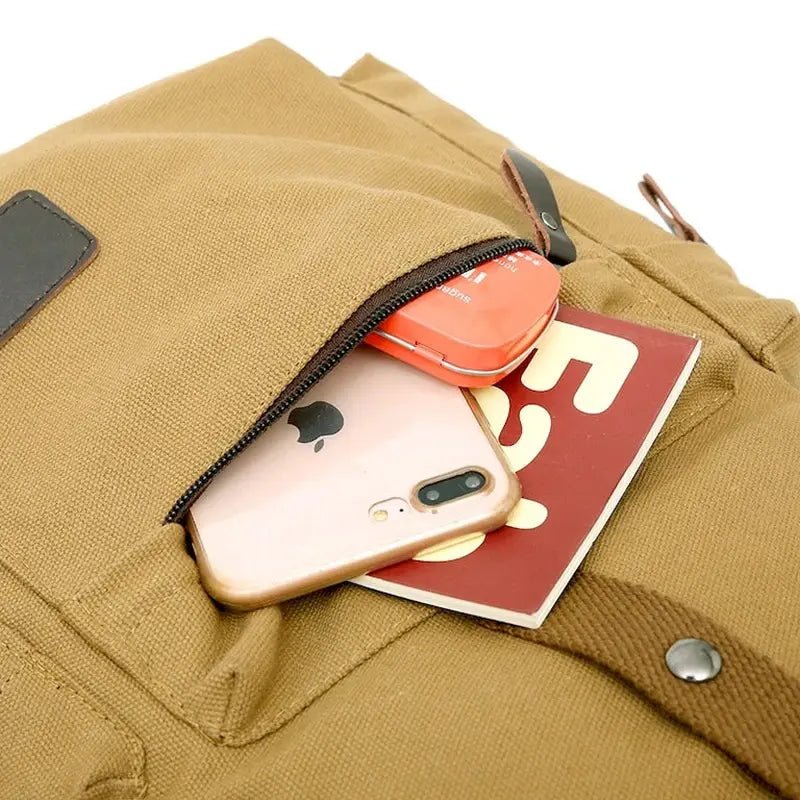 Sac à dos de voyage en toile tan avec poche zippée contenant smartphone, boîte rouge et petit livre