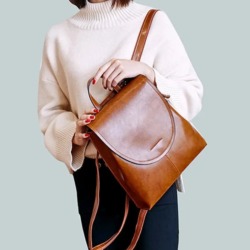 Femme en pull blanc et pantalon foncé tenant un sac à dos en similicuir brillant