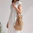 Femme portant une robe blanche avec un sac à dos en paille chic et tressée