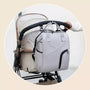 Sac à dos à langer chic gris clair avec plusieurs poches suspendu sur une poignée de poussette