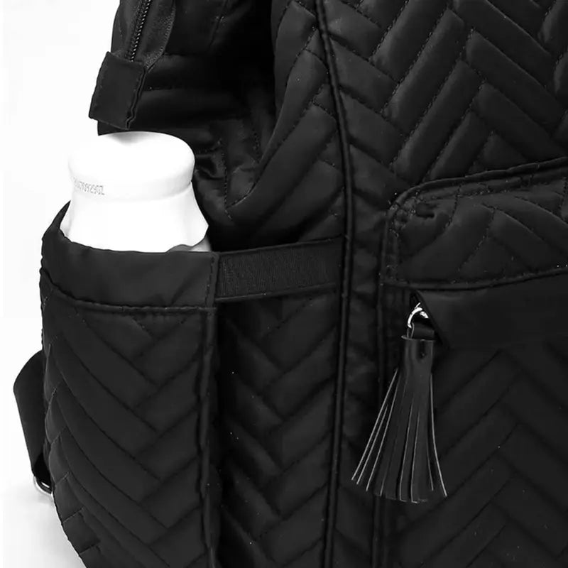 Sac à dos à langer design noir mat avec poche latérale contenant une bouteille blanche