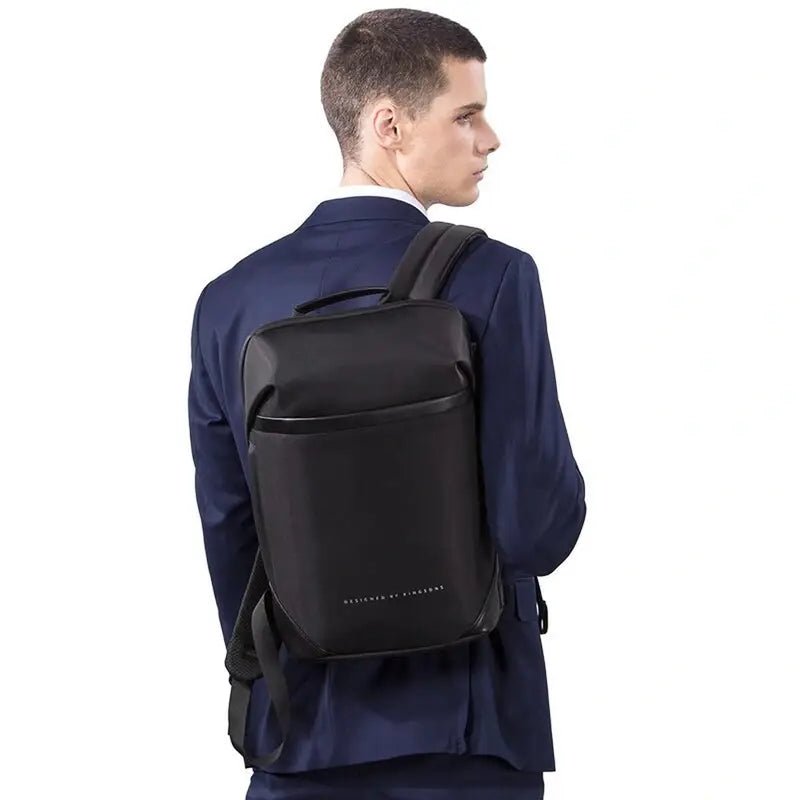 Sac à dos ordinateur portable plat et étanche noir porté sur l’épaule d’un homme en costume Navy