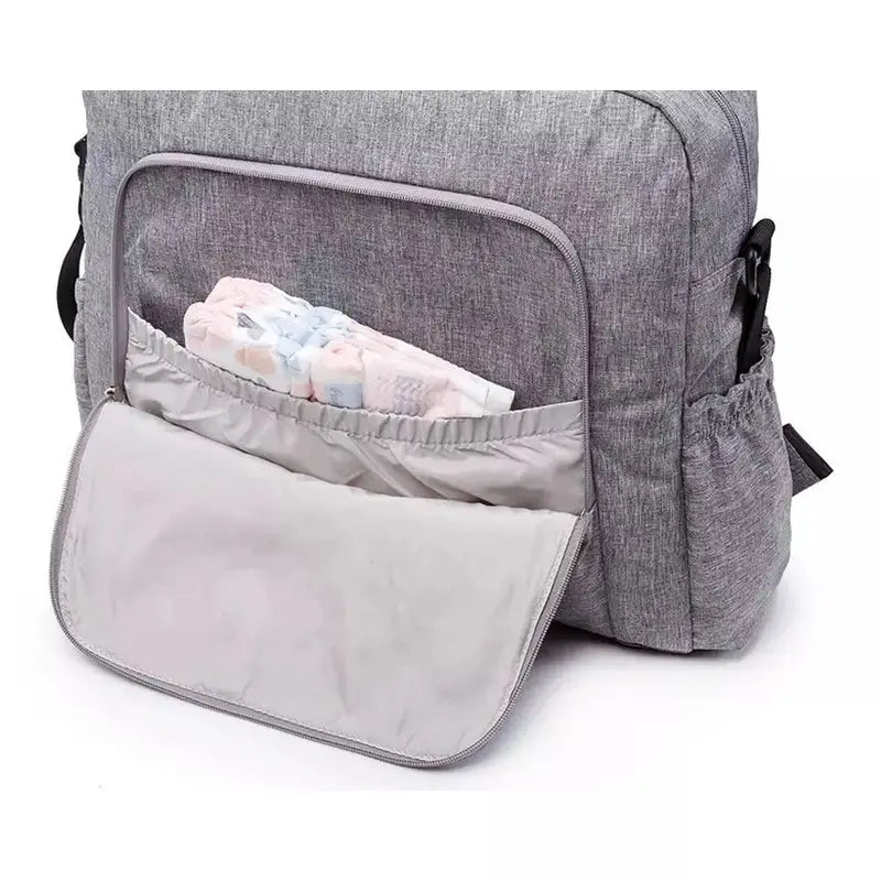 Sac à langer à dos en tissu gris avec poche frontale ouverte contenant des couches et un matelas à langer